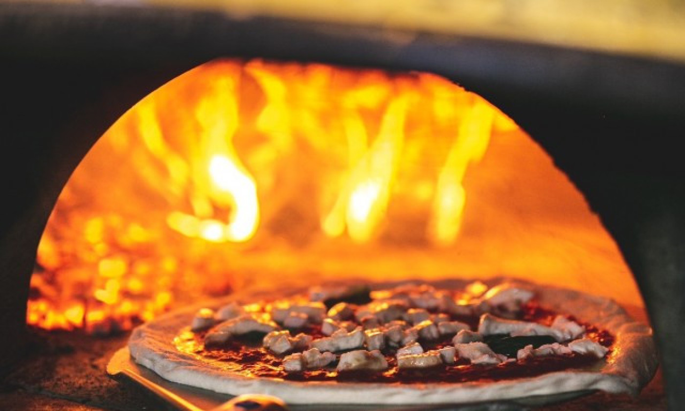 Une pizze en cuisson dans le four à bois, flammes vives.